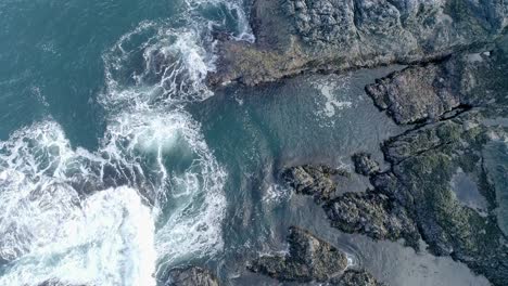 Rough-swirling-tidal-waters-wave-over-low-lying-rocky-coastline,-Rockpools-and-craggy-rocks-are-visible-against-the-shallow-turquoise-sea