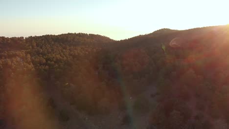 Drone-aerial-view-flying-over-mount-Olympus-with-bright-orange-glow-and-sun-flares