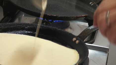 SLOMO:-Shot-of-a-cook-pouring-dough-in-a-frying-pan-to-make-pancakes-on-a-stove