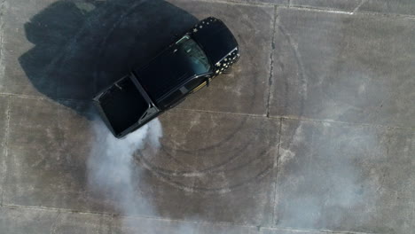 AERIAL:-Topshot-of-a-black-truck-doing-donuts-on-an-abandoned-parking-lot