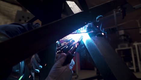 Worker-is-welding-metal-construction-in-the-factory,-there-are-sparks-in-the-shot