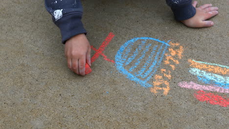 Young-boy-age-4-years-old,-drawing-on-sidewalk-with-chalk