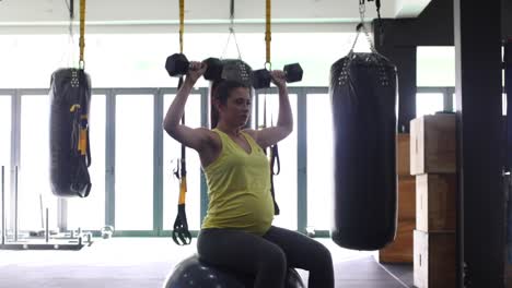 Pregnant-female-model-working-out-with-weights-in-a-gym-to-keep-fit-in-her-fourth-trimester