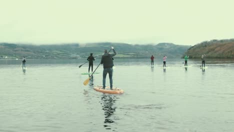 Crowd-of-paddle-boarders-stand-up-paddling-on-lake-within-nature