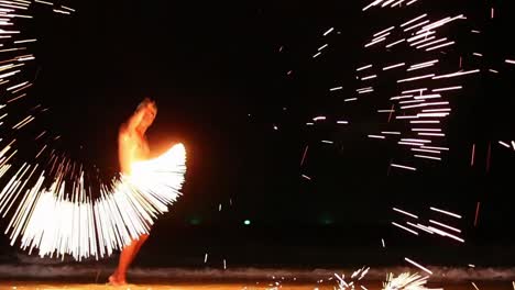 A-thai-man-dances-with-a-steel-wool-and-chains-in-a-fireshow-performance-until-he-creates-a-countless-amount-of-sparks-to-entertain-tourists-at-the-beach-of-Samet-Island,-Thailand