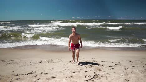 Young-man-in-red-shorts-comes-from-sea-in-a-beach