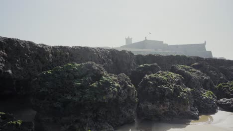 Nature-Sea-Ocean-Shore-Stones-Rocks-Waves-Sand-Seaweed-Sunny-Daylight-Clif-Fortress-Traveling-Tilt-Shot-4K