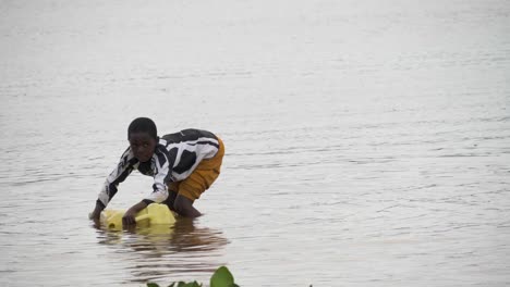 A-young-African-girl-collecting-water-from-a-yellow-jerry-can-in-Lake-Victoria