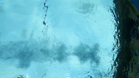 Underwater-angle-of-a-woman-wearing-swimwear-diving-into-a-blue-pool