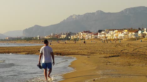 Junger-Mann-Läuft-Barfuß-Am-Ufer-Des-Sandstrandes,-Küstenstadt,-Spanien