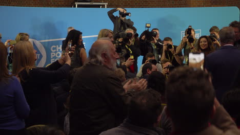 Brexit-Party-leader-Nigel-Farage-walks-towards-a-stage-full-of-press-photographers-and-the-audience-stand-up-and-applaud-at-a-press-conference-prior-to-the-General-Election