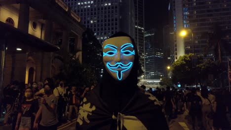 Empuje-Lento-De-Un-Manifestante-Con-Una-Máscara-De-Guy-Fawkes-Mientras-La-Multitud-Pasa,-Hong-Kong