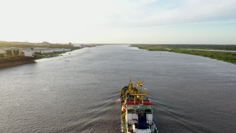 Aerial-Overtake-Shot-Of-Commercial-Ship-Sailing-Out-Of-Barranquilla-Port-On-The-Magdalena-River-During-Golden-Hour-Sunset