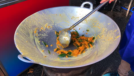 A-vendor-stir-frying-an-egg-yolks-into-a-large-wok-with-the-use-of-large-metal-ladle