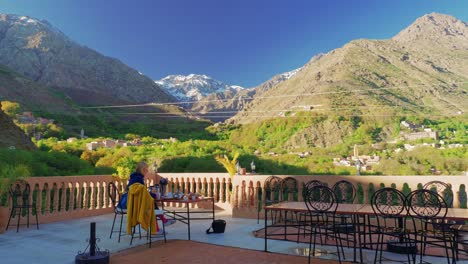 Tourist-eating-breakfast-at-the-rooftop-terrace-in-Imlil-with-Toubkal-view,-Morocco