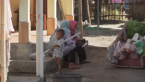 Small-child-playing-next-to-two-muslim-women-in-a-small-village-in-Indonesia