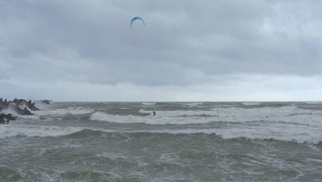 Kite-surfing-surfers-sailing-on-the-big-Baltic-sea-waves-at-Liepaja-Karosta-beach,-overcast-autumn-day,-slow-motion-wide-shot