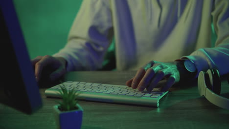 Hände-Eines-Männlichen-Arbeiters,-Der-Auf-Der-Tastatur-Tippt-Und-Mit-Einem-Computer-Auf-Einem-Grünen,-Farbenfrohen-Hintergrund-Arbeitet.-Nahaufnahme.