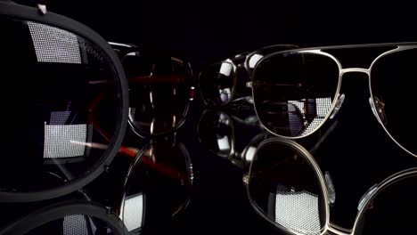 macro-view-moving-past-luxury-sunglasses,-Dolce-Gabbana,-Gucci,-Bvlgari,-Carrera,-ray-band,-probe-lens-view-4k-black-background
