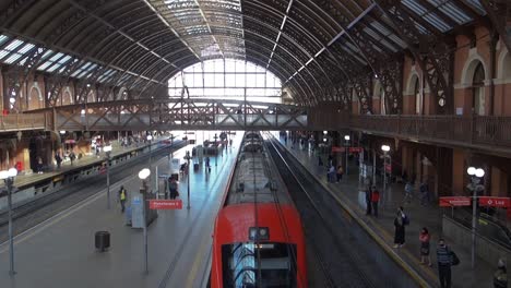 Tren-Saliendo-De-La-Estación,-Mientras-Los-Pasajeros-Esperan-En-La-Plataforma-De-Embarque