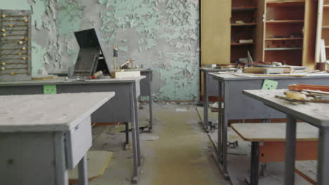 Walking-Inside-The-Abandoned-Classroom-Full-Of-Garbage-And-Rusty-Desk-With-Empty-Cabinet-Inside-The-School-Affected-In-Chernobyl-Exclusion,-Ukraine--wide-rolling