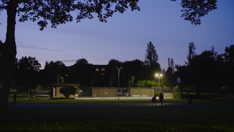 Nachtbasketball-Auf-Dem-Nachbarschaftsplatz-Spielen,-Während-Autos-Vorbeifahren