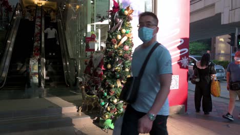 Pedestrians-wearing-face-masks-walk-past-a-flower-and-home-deco-products-shop-with-a-Christmas-tree-and-ornaments-displayed-at-its-entrance-in-Hong-Kong