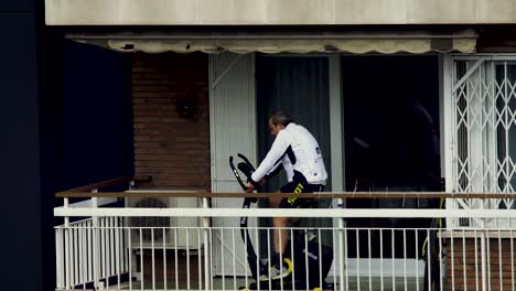 Man-during-quarantine-exercising-on-his-exercise-bike-on-his-balcony