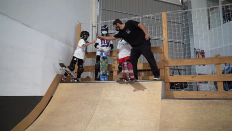 Adult-Skateboard-coach-giving-high-five-to-children-on-ramp-inside-skate-park