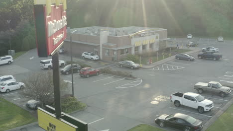 Drone-aerial-pull-back-of-McDonald's-restaurant-building-parking-lot-with-sign-at-sunrise-flying-in-reverse