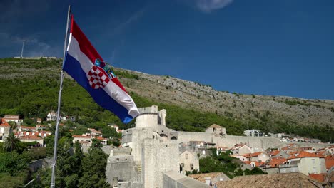 Toma-De-La-Bandera-Croata-Ondeando-En-La-Pared-En-El-Casco-Antiguo-De-Dubrovnik-Con-Mt-Srd-En-El-Fondo