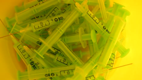 Green-syringes-in-a-yellow-recycling-recipient