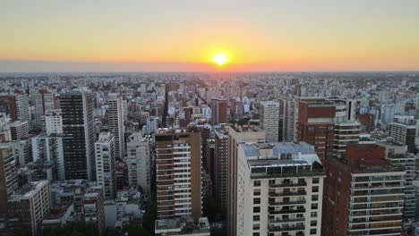Dolly-in-flying-over-Buenos-Aires-city-buildings-at-sunset-with-bright-sun-in-horizon,-Argentina