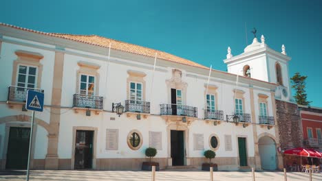 Portugal-Algarve-Loule-typical-square-city-hall-with-pedestrians,-cars-and-motorcycles-passing-by-at-morning-with-sunshine-4K