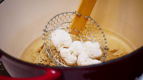 Lowering-breaded-cauliflower-into-frying-oil-with-spider-skimmer,-Slow-Motion