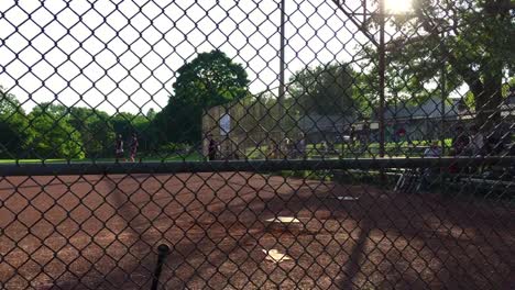 Wide-shot-through-the-fence-of-man-hitting-a-base-hit-and-running-to-first-during-a-community-baseball-game