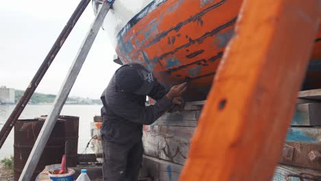 Fisherman-repairs-fishing-boat-with-water-proofing-sealant-slow-motion-shot
