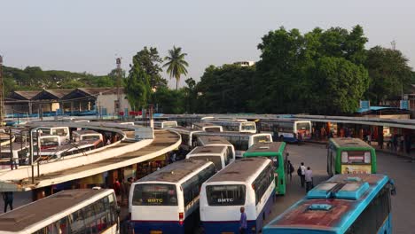 Luftaufnahme-Eines-Stapels-Von-Bussen,-Die-In-Den-Busbahnhof-Einfahren,-Und-Passagieren,-Die-Damit-Beschäftigt-Sind,-Die-Busse-Am-Majestätischen-Busbahnhof-Bengaluru,-Indien,-Zu-Bekommen