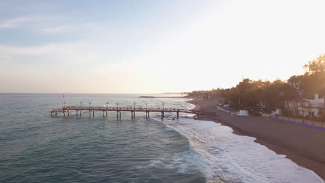drone-flying-towards-wooden-pier-in-ocean,-filmed-in-marbella,-malaga,-spain