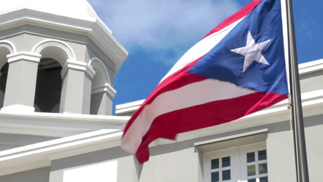 Bandera-Puertorriqueña-Ondeando-En-El-Viento-Mientras-Una-Paloma-Sale-Volando-De-La-Torre-De-Un-Edificio