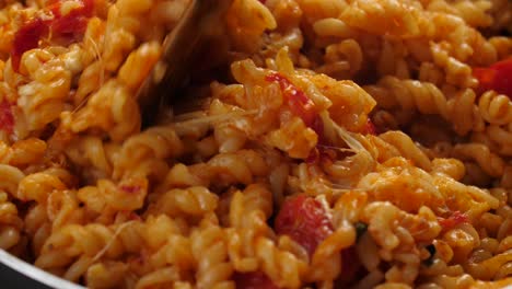 Mouthwatering-close-up-shot,-stirring-creamy-and-cheesy-pasta-with-tomato-sauce-using-wooden-spatula,-stretching-melted-mozarella-cheese