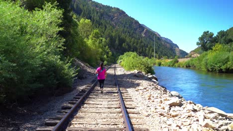 Middle-aged-woman-walks-on-railroad-tracks-along-river-in-a-canyon