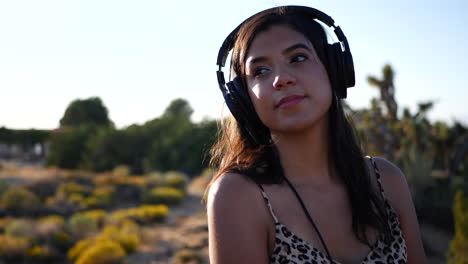 Eine-Schöne-Hispanische-Frau,-Die-Musik-über-Ihre-Kopfhörer-Hört-Und-Vor-Glück-Im-Freien-In-Zeitlupe-In-Der-Natur-Lächelt