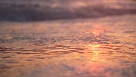 Slow-motion-close-up-of-small-wave-running-back-into-the-ocean-at-the-beach-with-bubbles-at-sunset