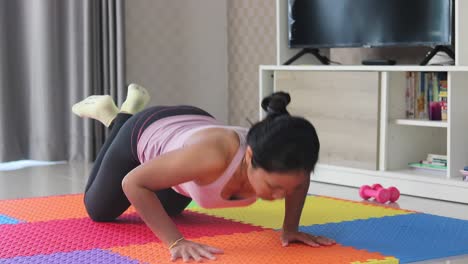 Slim-young-asian-woman-is-working-out-on-a-floor,-doing-push-up-exercise-in-her-living-room