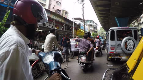 Rickshaw-driving-in-busy-city-street-with-scooters,-bicycles,-and-cars