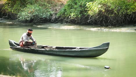 Person-uses-net-on-a-canoe-to-fish-in-green-water-river,-slow-motion