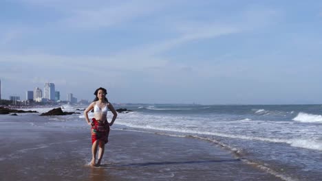 Junge-Asiatische-Frau-Geht-Am-Strand-In-Vietnam-Spazieren,-Mit-Der-Skyline-Der-Stadt-Im-Hintergrund