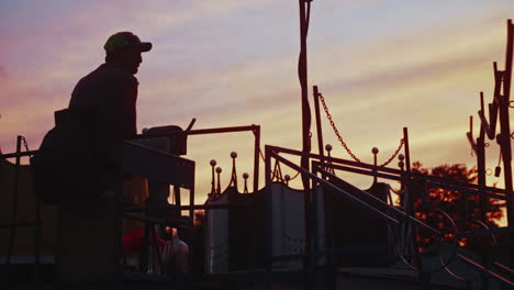 Carnival-worker-watching-ride-spin-at-sunset,-Medium-Shot,-Slow-Motion