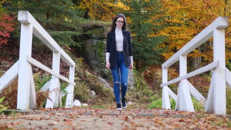 Teenage-Girl-in-a-Casual-Clothes-Walking-Over-Bridge-in-Colorful-Park-on-Autumn-Day,-Slow-Motion